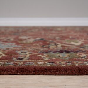High-pile traditional rug border in reddish-brown resting on light wood floors against a gray wall.