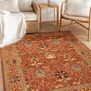 A terracotta traditional rug featuring blue, gold, and beige florals is placed under rattan furniture.