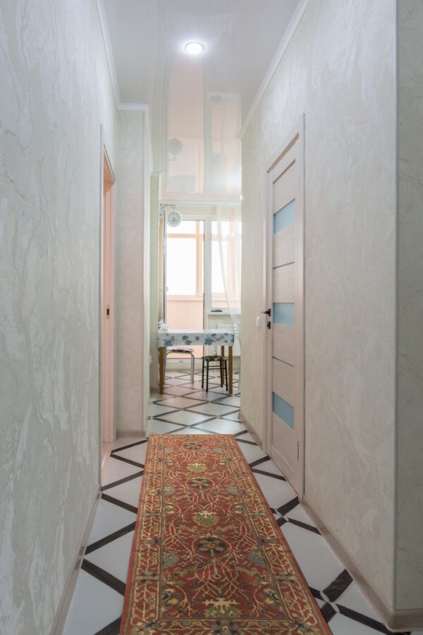 A red traditional runner rug with detailed patterns is centered on geometric black and white tile in a bright hall.