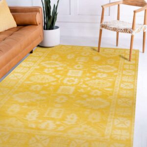 Low-pile yellow rug with a distressed traditional pattern sits between a leather sofa and a light wooden chair.