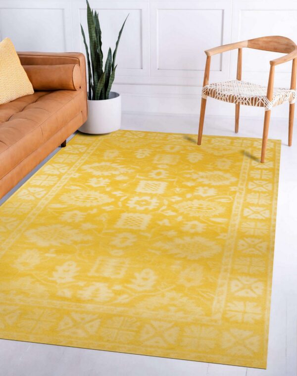 Low-pile yellow rug with a distressed traditional pattern sits between a leather sofa and a light wooden chair.