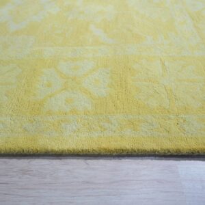 Yellow medium-pile rug with a subtle floral pattern rests on light wood floor planks.