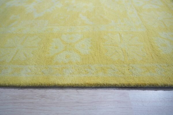 Yellow medium-pile rug with a subtle floral pattern rests on light wood floor planks.