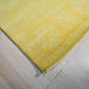 Close-up of a textured yellow rug with a subtle pattern lying on light wood flooring.