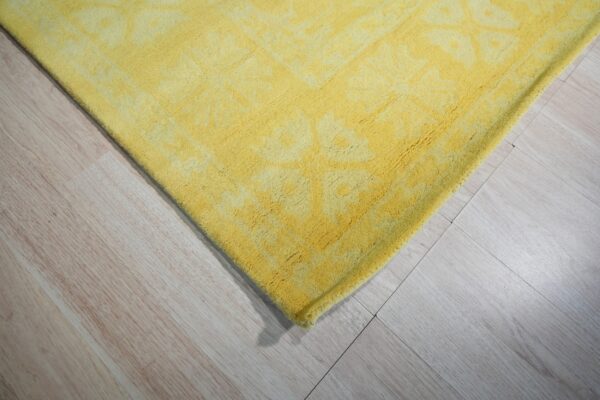 Close-up of a textured yellow rug with a subtle pattern lying on light wood flooring.