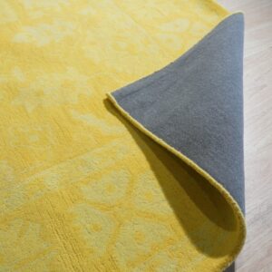 Tonal yellow high-pile rug with a lifted corner exposing the gray backing on pale wood floor.