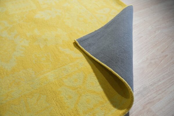 Tonal yellow high-pile rug with a lifted corner exposing the gray backing on pale wood floor.