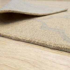 Rolled edge of a beige textured rug with a subtle gray pattern rests on light wood planks.