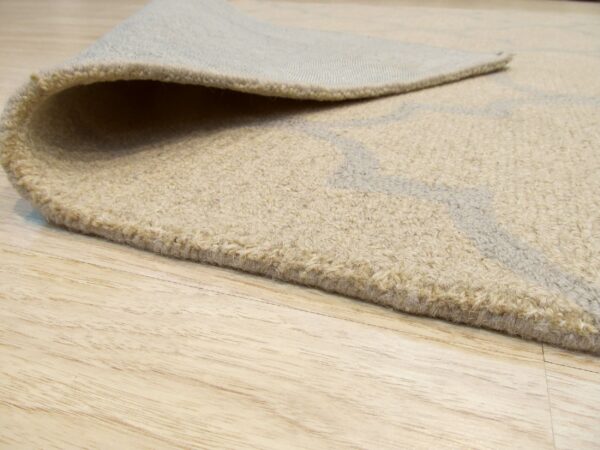 Rolled edge of a beige textured rug with a subtle gray pattern rests on light wood planks.