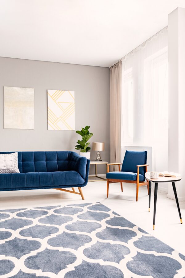 Blue rug with a bold white geometric pattern sits below a navy blue sofa and armchair in a bright room.