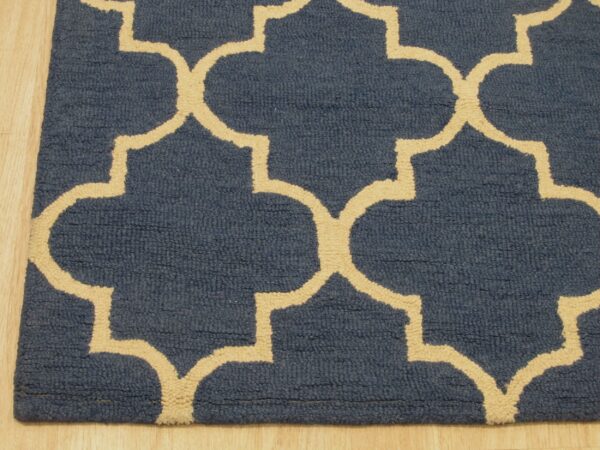 Close-up of a navy blue rug with a beige geometric trellis pattern on light wood flooring.