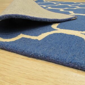 Close-up showing a medium pile blue rug with cream trellis pattern and woven backing on light wood floor.
