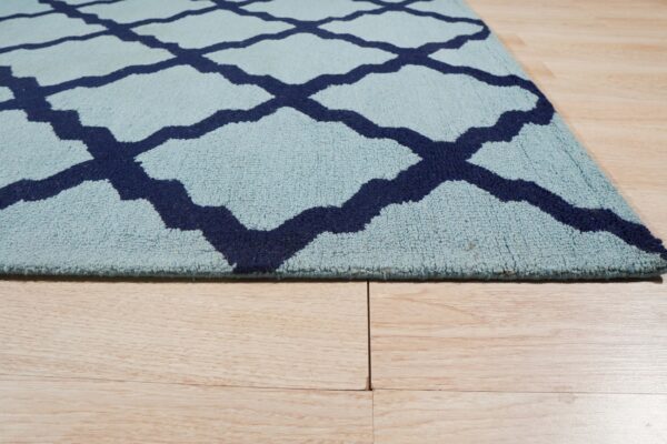 Light blue, medium-pile rug with a navy geometric trellis pattern rests on light wood plank flooring.