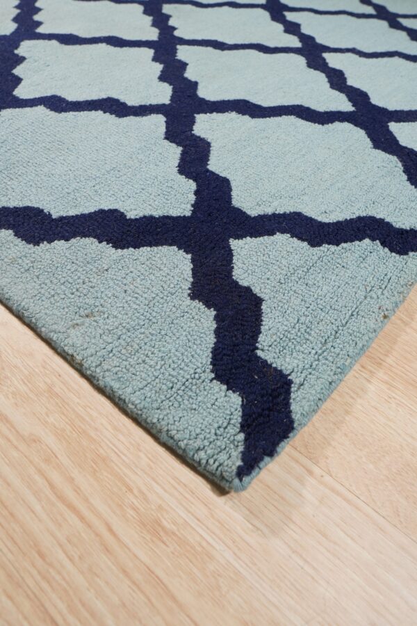 Light blue rug with navy trellis pattern and textured pile on natural wood plank flooring.