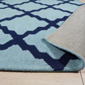 Light blue rug with navy trellis pattern is rolled back, revealing its woven gray backing on wood floor.