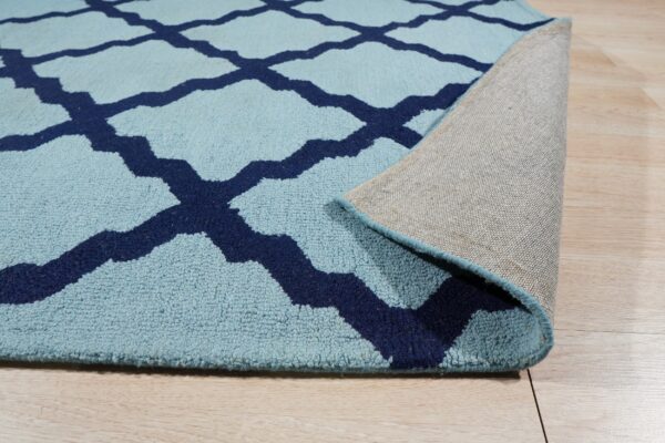 Light blue rug with navy trellis pattern is rolled back, revealing its woven gray backing on wood floor.