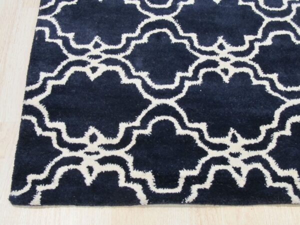Navy blue rug with a white moroccan trellis pattern rests on light wood flooring.