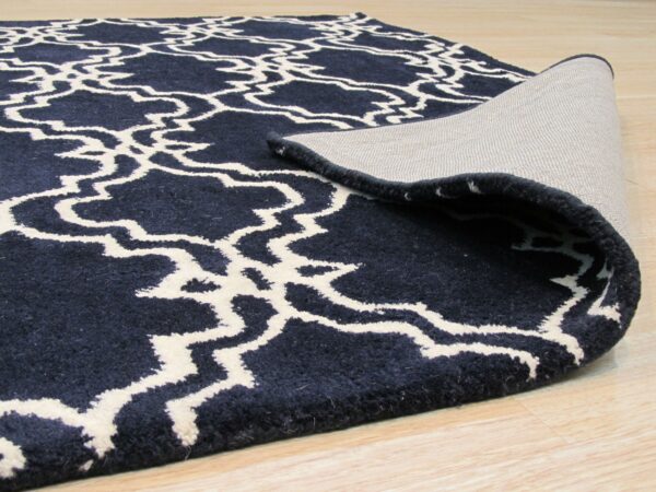A navy high-pile rug with a cream trellis pattern is rolled back, showing the woven backing on light wood floors.