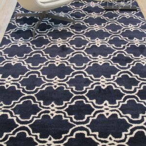 A navy and white quatrefoil rug on wood flooring sits beneath a modern white chair and decor.