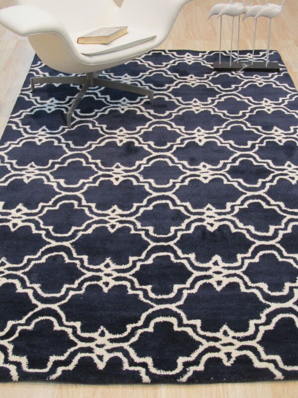 A navy and white quatrefoil rug on wood flooring sits beneath a modern white chair and decor.