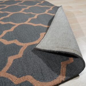 Charcoal gray rug with a peach trellis pattern is curled back showing its woven backing on a light wood floor.