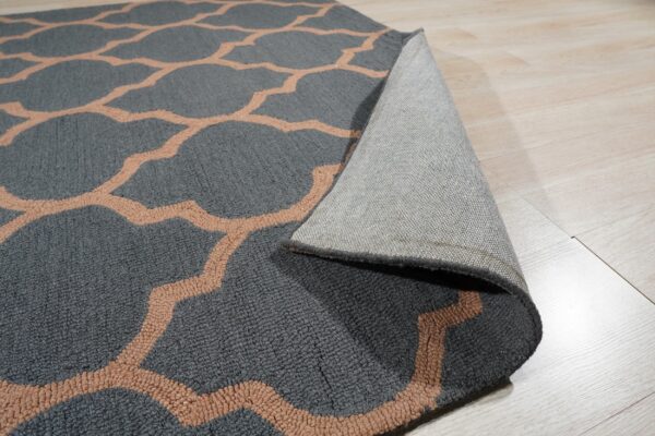 Charcoal gray rug with a peach trellis pattern is curled back showing its woven backing on a light wood floor.