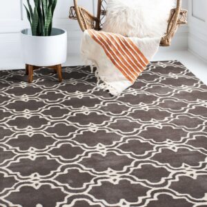 A brown and cream geometric trellis rug grounds a wicker chair and a tall potted plant on a white floor.