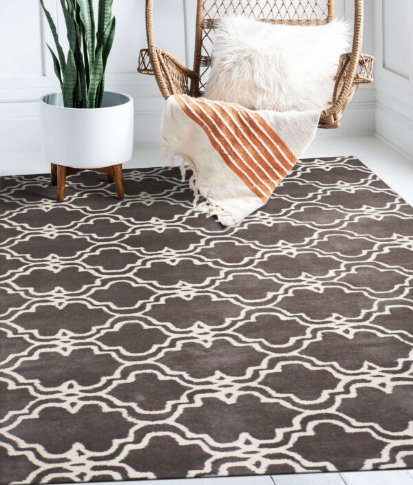 A brown and cream geometric trellis rug grounds a wicker chair and a tall potted plant on a white floor.