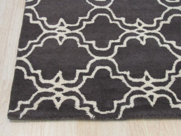 Close-up of a charcoal rug with a creamy white moroccan quatrefoil pattern on light wood flooring.