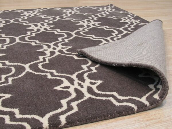 A textured dark brown rug with a cream geometric pattern is folded over on light wood flooring.