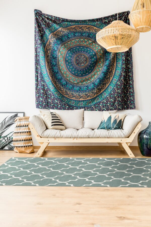 A low-pile teal rug with a white quatrefoil pattern is beneath a light wood sofa and woven pendant lights.