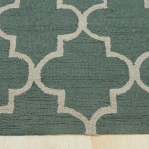 Cut pile teal rug with a light beige geometric lattice pattern rests on light blonde wood flooring.