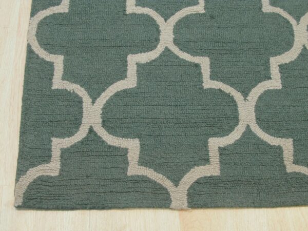 Cut pile teal rug with a light beige geometric lattice pattern rests on light blonde wood flooring.