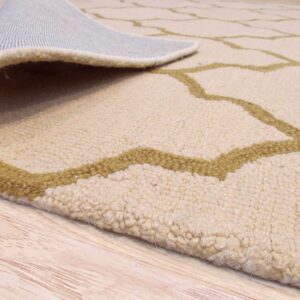 High-pile beige rug with olive trellis pattern curled up, showing its backing on blonde wood.