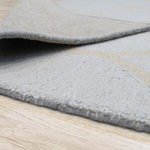 The textured light gray rug with beige pattern has a woven backing visible on light wood planks.