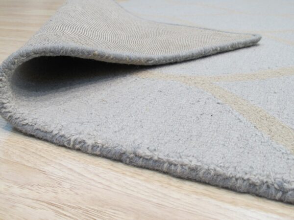 The textured light gray rug with beige pattern has a woven backing visible on light wood planks.