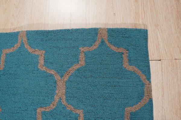 Textured teal rug with a tan geometric pattern rests on light wood plank flooring.