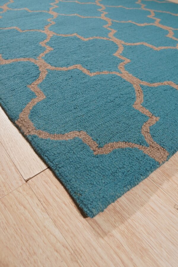 Textured teal rug with a tan geometric trellis pattern on light wood flooring.