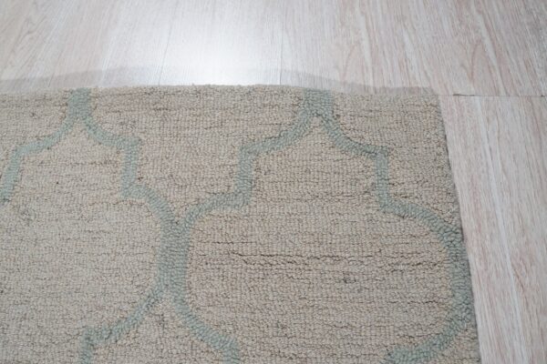 A textured beige rug with a light gray-blue geometric pattern rests on light wood plank flooring.
