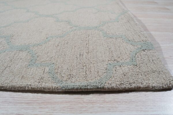 Textured, thick pile beige rug with a pale aqua trellis pattern on light wooden floorboards.
