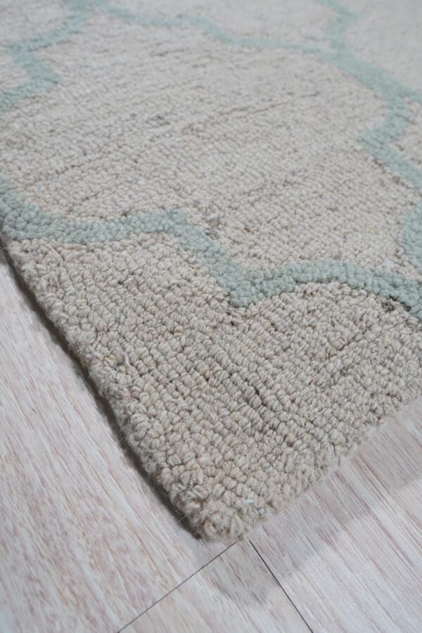 Textured beige rug with a pale blue geometric pattern rests on light wood grain flooring.