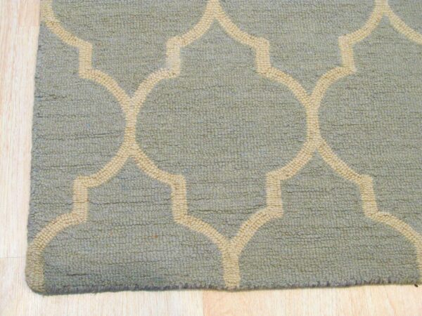 Close-up of a blue-green textured rug featuring a raised beige moroccan trellis pattern on light wood floor.