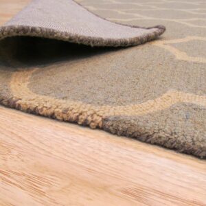 Muted green and beige patterned rug with visible pile and woven backing rests on wooden floor.