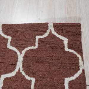 Nubby, rust-brown rug with a thick white ogee pattern shown on light plank flooring.