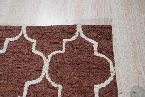 Nubby, rust-brown rug with a thick white ogee pattern shown on light plank flooring.