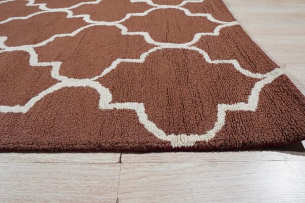 Close view of a brown looped rug with a cream ogee pattern lying on light wood planks.