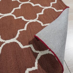 Close-up of a high-pile, rust and white quatrefoil pattern rug with the edge folded back revealing a backing.