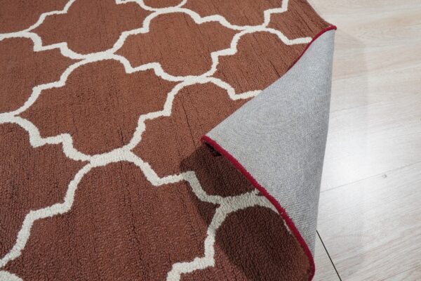 Close-up of a high-pile, rust and white quatrefoil pattern rug with the edge folded back revealing a backing.