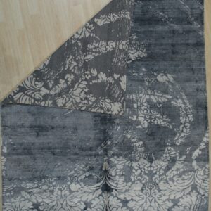 Dark gray distressed floral rug lying on light wood planks, showing the patterned woven backing.