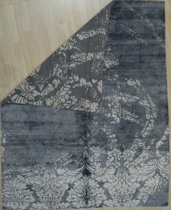 Dark gray distressed floral rug lying on light wood planks, showing the patterned woven backing.